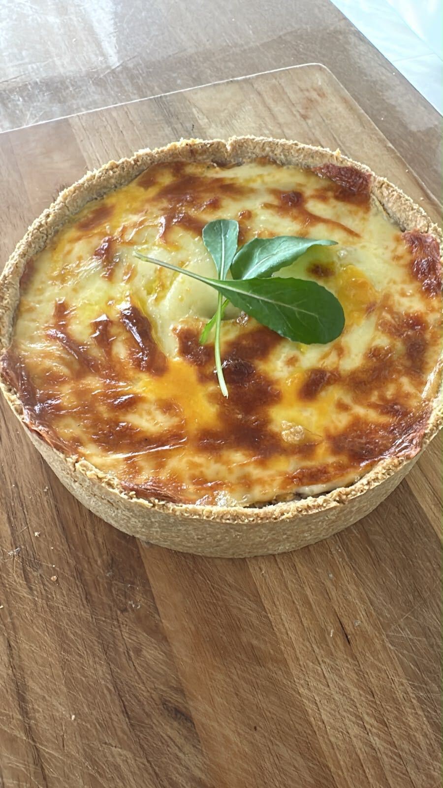 Torta artesanal gratinada, vista de cima, com folha de rúcula sobre a cobertura dourada